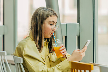 Teenage girl using phone and drinking juice in school cafeteria
