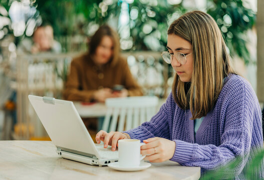 Girl holding coffee cup using laptop sitting at school cafeteria