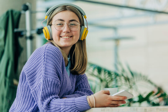 Happy teenage girl wearing bluetooth headphones at school cafeteria
