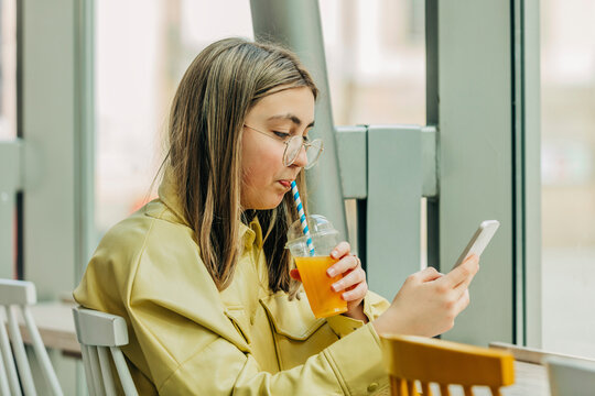 Teenage girl using phone and drinking juice in school cafeteria