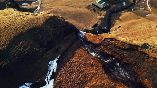 Arctic cascade falling down off cliff, foss a sidu waterfall with river flow running off frozen hills in icelandic landscape. Spectacular water stream in nordic nature and wilderness. Aerial view.