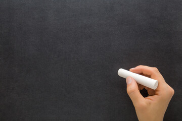 Young adult woman hand holding white chalk stick and writing on black dark chalkboard wall...