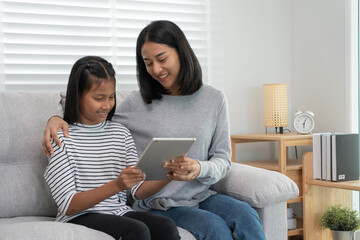 Obraz premium Mother teaching lesson for daughter by tablet. Mother and child laughing happily. Do homework with kind mother help, encourage for exam. Asia girl happy Homeschool. Mom advise education together.