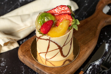 Cream cake covered with fruit and chocolate. Fruit cake on a dark background