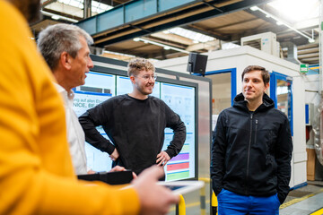 Smiling employee with hands in pockets attending meeting at factory