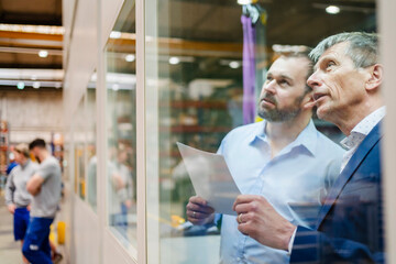 Businessman and manager discussing over document seen through glass window at factory