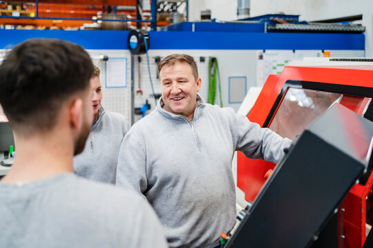 Smiling employee with colleagues by CNC machine at factory