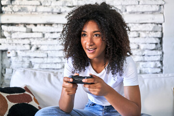 Joyful young woman plays video game on sofa, immersed in fun.