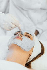 Obraz na płótnie Canvas A professional cosmetologist applies a cosmetic mask to moisturize and cleanse the skin on a woman's face at a beauty session in a spa. Beautician performs therapy on the face with a cosmetic mask