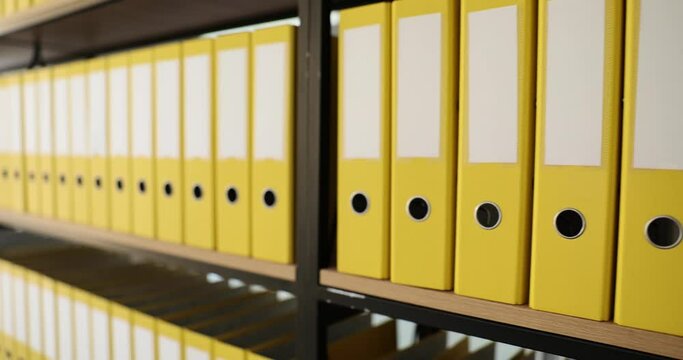 Yellow identical folders with materials and documents are arranged in rows on shelves. Storage of business documents