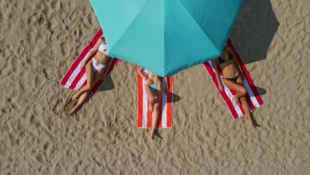 Three young women lying on the beach, dancing, sunbathing in swimming suites, relaxing and enjoying.