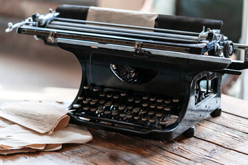 Vintage aged black typewriter with old paper blank on wooden table. Retro style photo.