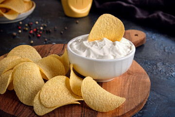 Beautiful potato chips and white sauce bowl. On a dark blue abstract background.