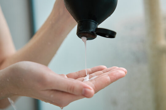 Pouring shampoo from bottle on female hand in bathroom. Hygiene concept