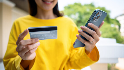 Cropped image of happy young woman holding credit card, paying bill with online payment via internet on smart phone