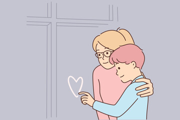 Mother hugs son draws heart on window sweaty in cold winter weather for family happiness concept