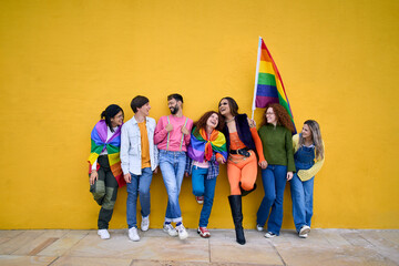 Portrait of group cheerful young friends standing on wall yellow. LGBT community smiling people on gay pride day enjoying together and showing rainbow flags. Generation z and parade party homosexual. - obrazy, fototapety, plakaty