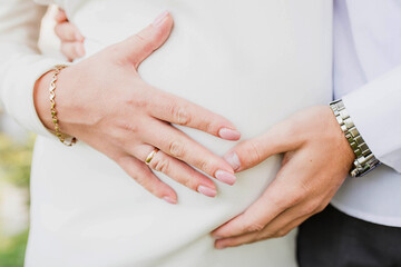 a man and a woman hold on to a big belly at a wedding, a symbol of pregnancy and love