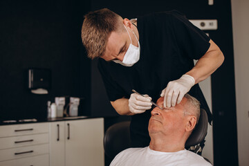 A plastic surgeon examines an older gray-haired man