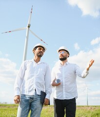 Two engineers discussing against turbines on wind turbine farm.