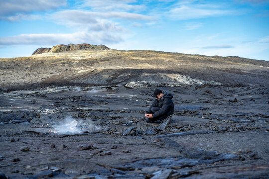 man taking a picture with a phone of a drone on lava field at icelandic Fagradalsfjall volcano with steam rising from under the lava