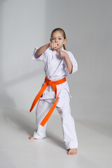 A little girl in a white kimono makes a punch with her hand.
