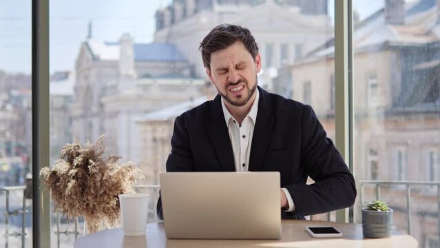 Handsome businessman working on laptop in cafe with city background feeling stomach pain, gastritis symptom, peptic ulcer, pancreatitis. Male it programmer suffering from digestive problems indoor.