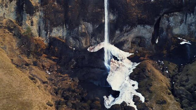Aerial view of foss a sidu cascade in iceland running off of hills forming scandinavian landscape, nordic scenery. Beautiful icelandic waterfall flowing down snowy mountains. Slow motion.
