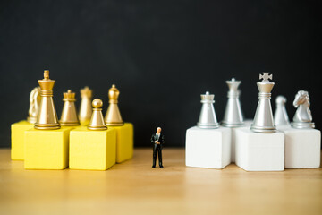 Miniature businessman standing on the center a wooden block with many of golden and silver color chess. The concept of business analysis and strategy. Stepping into the startup, new business player