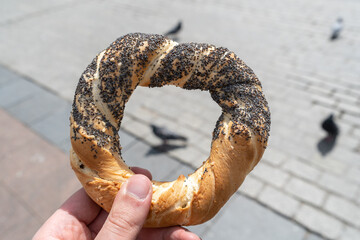Hand holding obwarzanek krakowski pretzel on Cracow Main Square Market, with pigeon bird in...