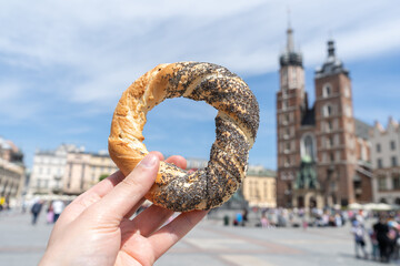 Hand holding obwarzanek krakowski prezel on Cracow Main Market Square. St. Mary's Basilica,...