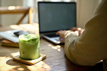 Close-up image of a glass of iced matcha green tea on a wooden table in a minimal cafe