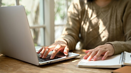 Cropped image of a female using her laptop and working on her tasks while sitting in a cafe.