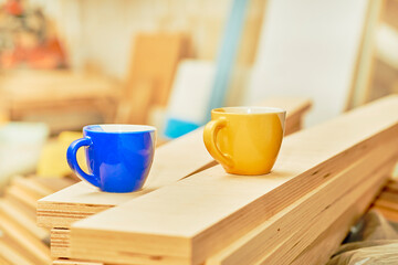 Work break, tea coffee time. Blue and yellow cups in carpentry on wooden planks