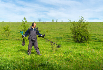 Fototapeta na wymiar A man with a metal detector with his back to the camera. Man in sportswear with a metal detector. Digger on a summer meadow. The concept of searching for coins underground. Digger with metal detector