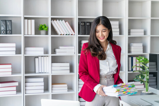 Asian happy beautiful businesswoman hold paper documents work stand at workplace. Attractive female employee office worker smile.