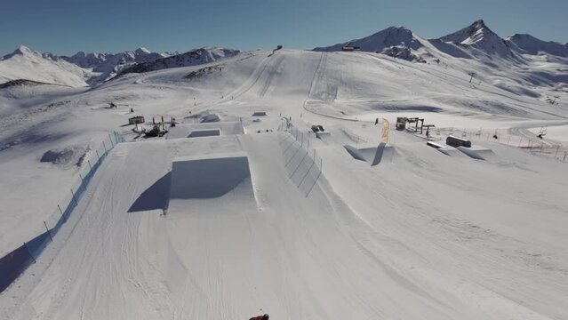 FPV Aerial View of Freestyle Skier Making Twists and Flips From Kickers in Snowpark on Sunny Winter Day 50fps