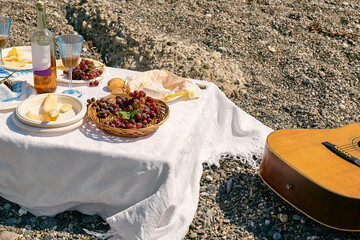 Summer beach picnic. Appetizers, fresh fruit, grape, yellow melon, bread, cheese and wine on white tablecloth outdoors at seaside at the beach.