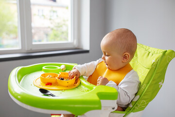 Dirty baby girl eats quinoa porridge and banana while sitting on high chair. Baby feeding concept.