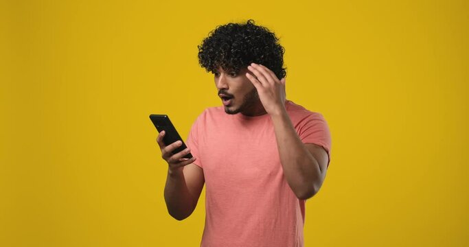 Young indian man using mobile cell phone typing then looking at camera surprised, frustrated and disappointed
