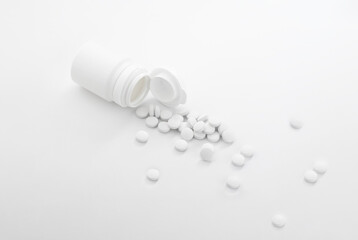 White pills spilling out of white bottle on light gray background.