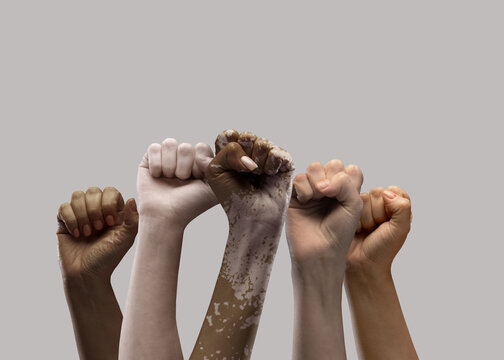Hands of different people, of diverse race, skin color, gender raising fists up over grey background. Human rights and equality. Concept of human relation, community, togetherness, symbolism, culture