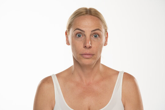 Portrait of a senior woman without make up and lifted eyebrows. Close up face of a mature blonde woman on a white background.