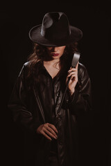 Fototapeta na wymiar woman in a leather raincoat and hat with a whip flogger for BDSM sex with submission and domination
