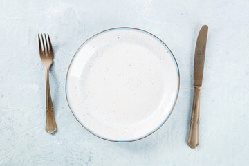 An empty white plate with a blue rim, with a fork and a knife, overhead flat lay shot on a slate background, the concept of dinner