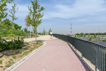 A person jogging on a walkway with red brick pavement and metal railing in a new urban park