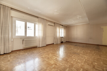 A large empty room in a house with parquet floors, several windows with curtains