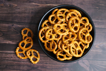 Crunchy pretzels in a black bowl are placed on a wooden table. A perfect salty party snack. copy space. crispy baked salt cookies or biscuits 