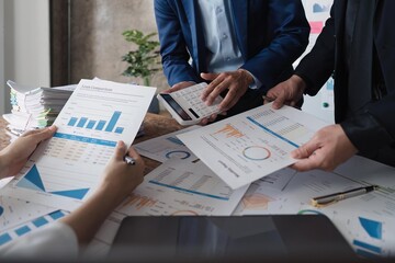 Business team using a calculator to calculate the numbers of statistic business profits growth rate on documents graph data, desk in the office, teamwork process