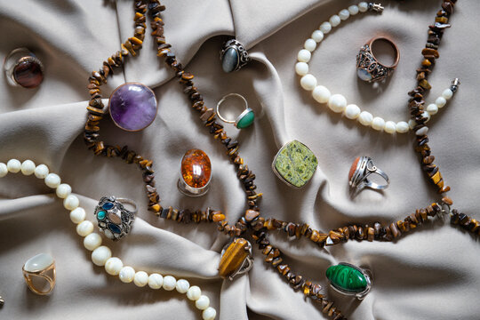 Many different silver rings and necklace with various natural gemstones over background.